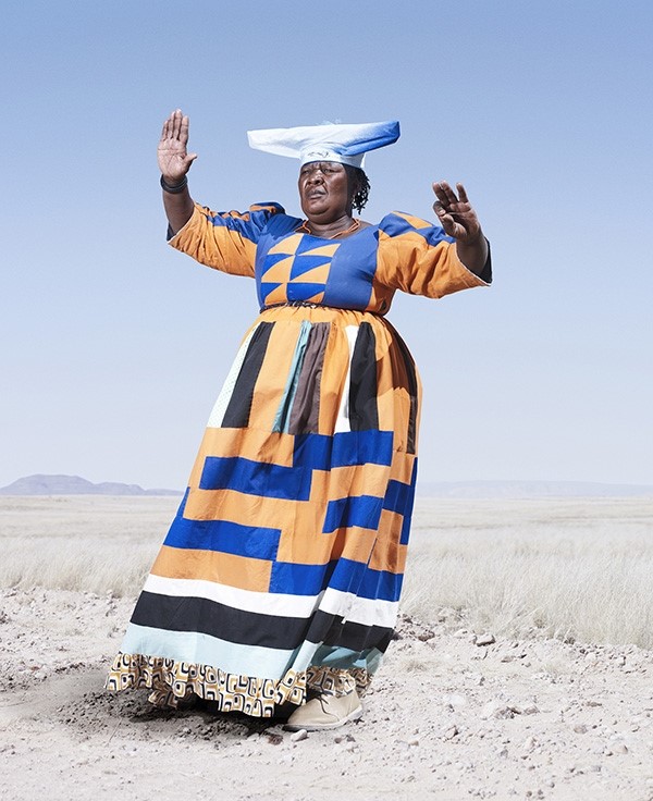 Herero woman in orange dress in cow dance pose