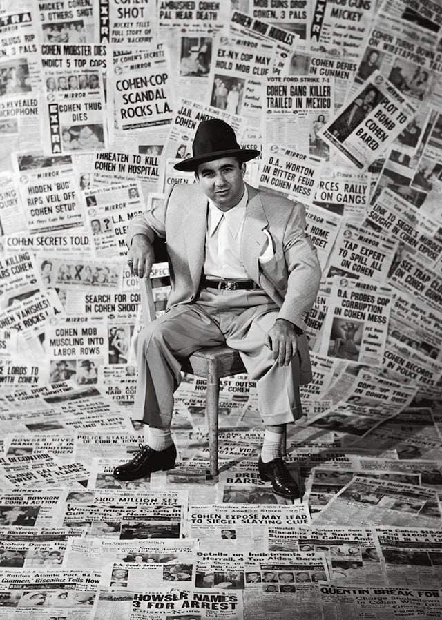 The gangster Mickey Cohen sitting amid the front pages of ne
