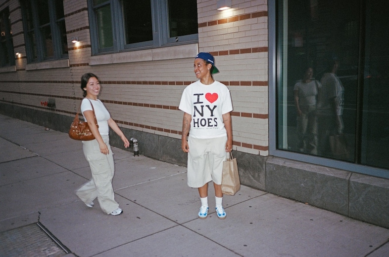 Film photography of two people on an urban sidewalk at dusk, lit by artificial street lighting.